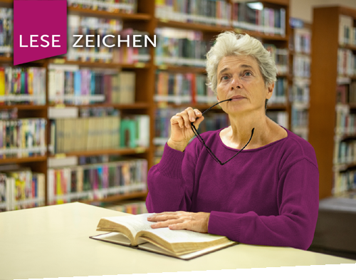 Titelbild der Literaturtage LeseZeichen 2025 - es zeigt eine Frau, sitzend am Tisch in der Bibliothek. Sie hat ein Buch aufgeschlagen und lässt ihren Blick noch oben schweifen. Links oben in der Ecke des Bild befindet sich das Logo Literaturtage LeseZeichen.