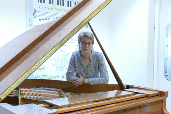 Das Bild zeigt Heide-Lore Neumann stehend am Klavier. Sie ist Musiklehrerin für Klavier und Korrepetition an der Musikschule Mittelsachsen.