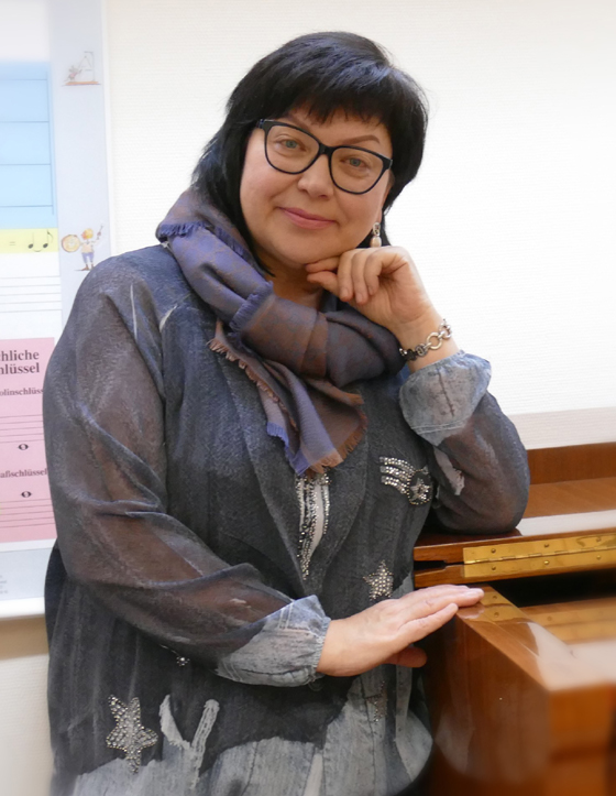 Das Bild zeigt Natalia Schreiner stehend am Klavier. Sie ist Musiklehrerin für Klavier und Gesang an der Musikschule Mittelsachsen.