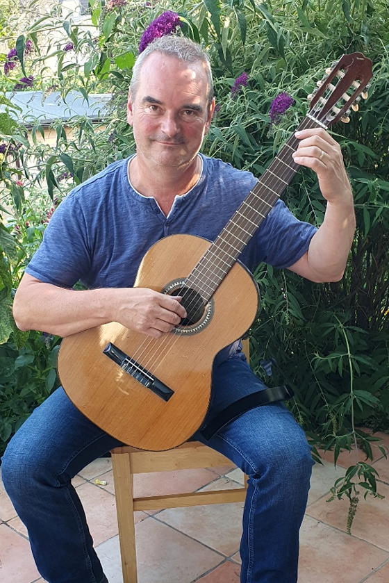 Das Bild zeigt Olaf Würzner sitzend auf einem Stuhl mit seiner Gitarre. Er ist Musiklehrer für Gitarre an der Musikschule Mittelsachsen.