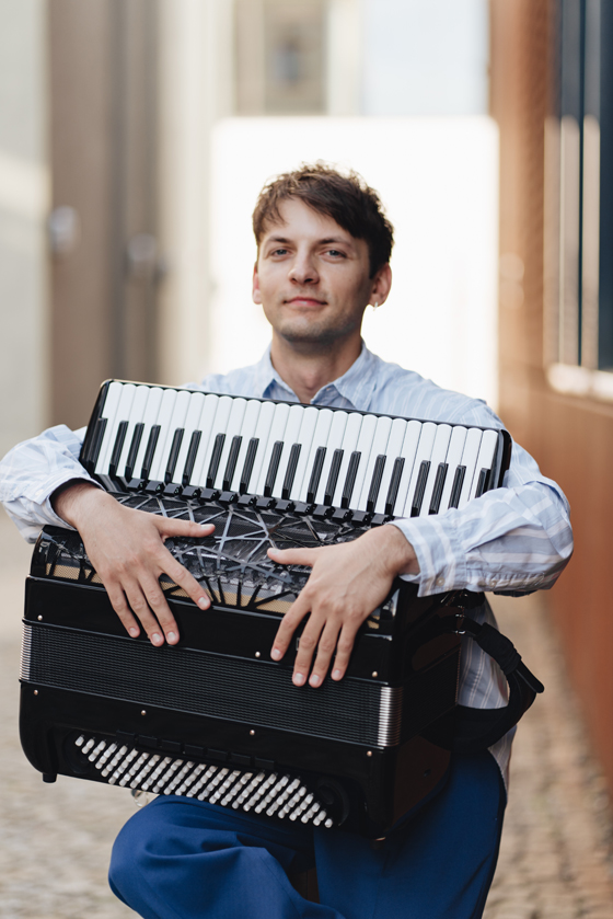 Das Bild zeigt Pavel Klinko mit seinem Akkordeon stehend in einer verlassenen Fabrikhalle. Er ist Musiklehrer für Akkordeon an der Musikschule Mittelsachsen.