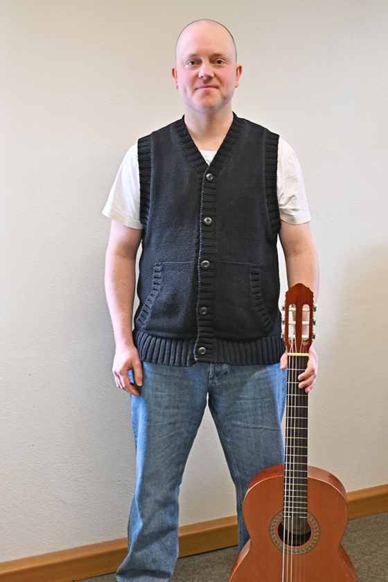Das Bild zeigt Frederik Kleimann stehend mit seiner Gitarre. Er ist Musiklehrer für Gitarre, E-Gitarre, E-Bass, Kontrabass an der Musikschule Mittelsachsen.